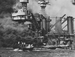 A small boat rescues a seaman from the 31,800-ton USS West Virginia burning in the foreground at Pearl Harbor, December 7, 1941