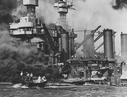 A small boat rescues a seaman from the 31,800-ton USS West Virginia burning in the foreground at Pearl Harbor, December 7, 1941