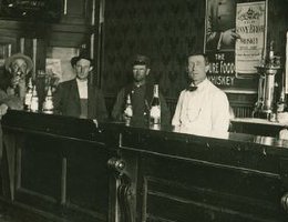Bar scene interior with six men including the bartender. The poster on the mirrored back bar advertises James C. Dahlman for Governor.